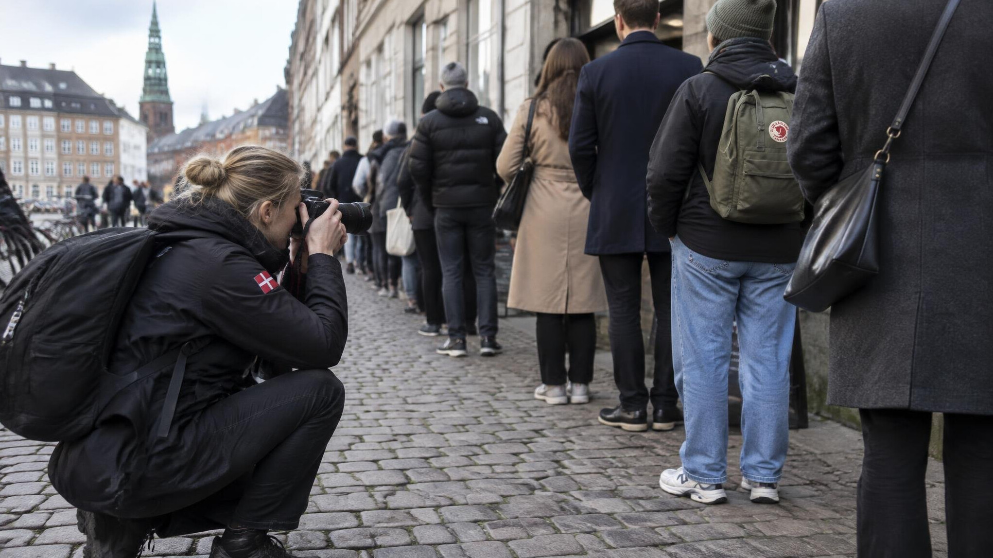 A photographer crouching to photograph people waiting in a queue